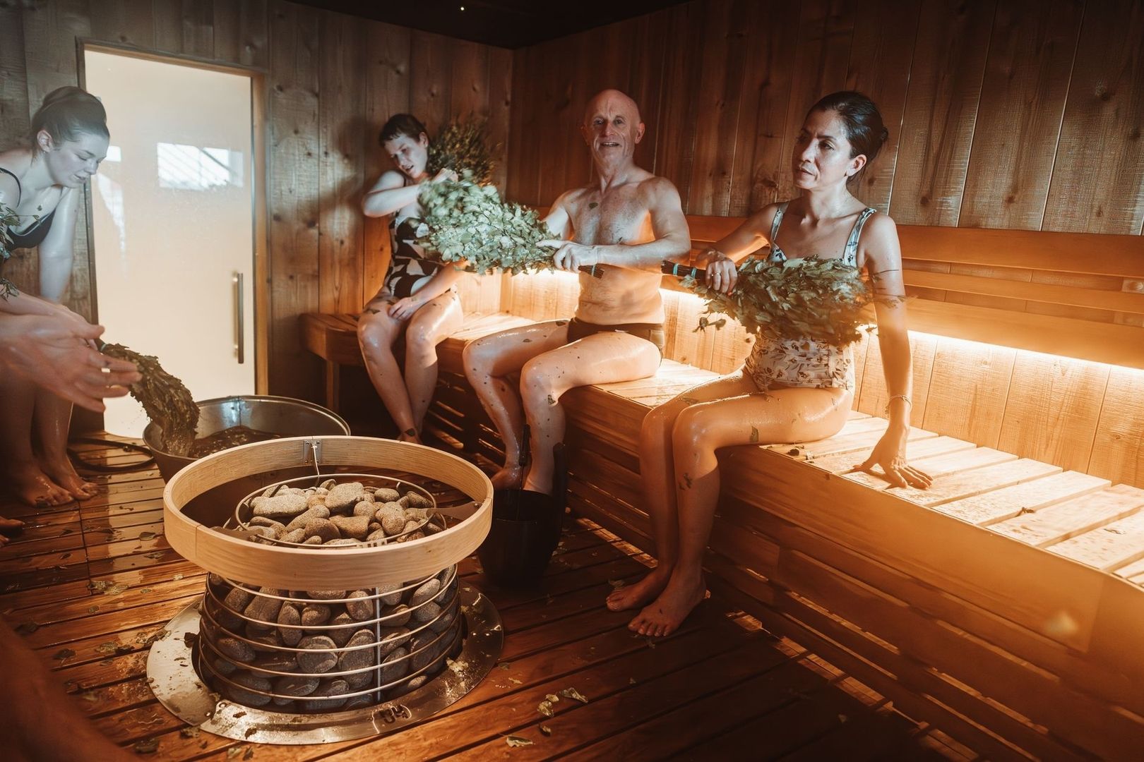 Vier mensen in een houten banya met berkenveniki en saunakachel